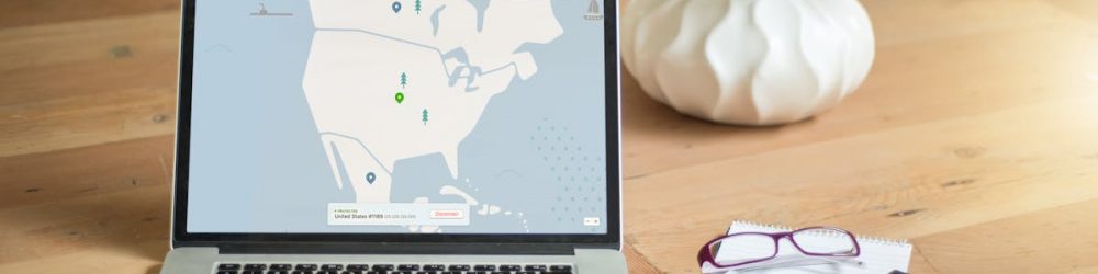 A laptop displaying VPN software sits on a wooden desk with a notepad and plant offering a secure workspace vibe.